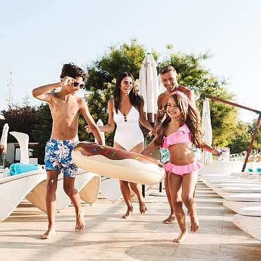 Eine junge Familie mit zwei Kindern ist im Urlaub glücklich und ausgelassen auf dem Weg zwischen Pool und Hotel
