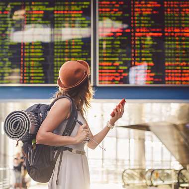 Jung Frau mit rotem Hut dreht sich am flughafen um zur Anzeige mit stornierten Flügen - Reise Storno Versicherung