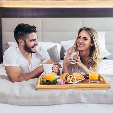 Junges Paar im Hotelbett beim Frühstück