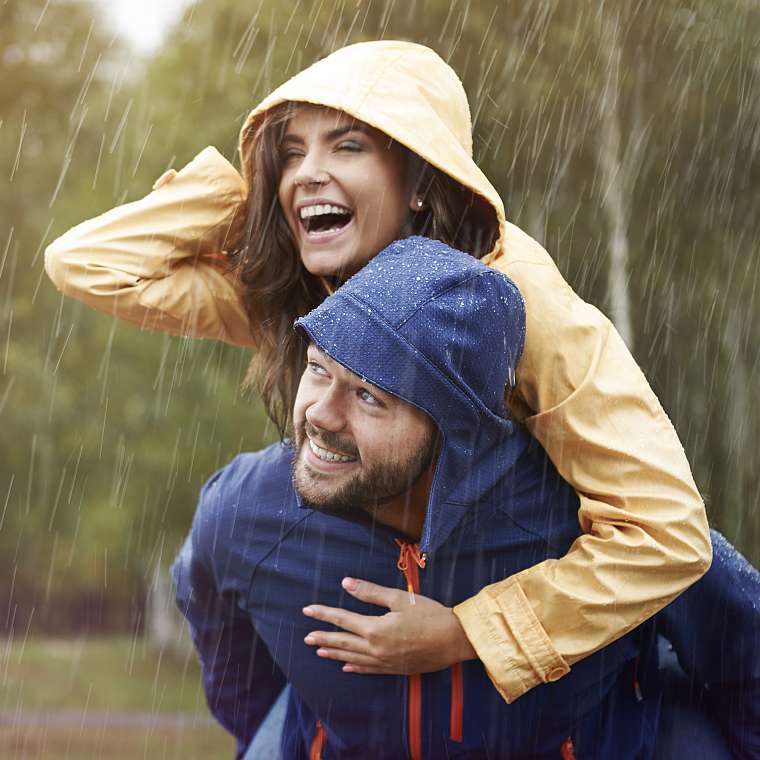 Junger Mann nimmt seine Frau im Regen Huckepack und beide sind dabei ausgelassen frÃ¶hlich